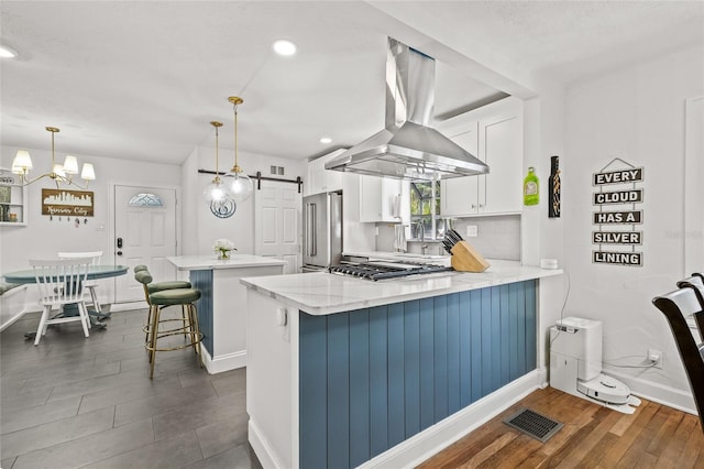 kitchen featuring a barn door, stainless steel appliances, visible vents, white cabinetry, and range hood