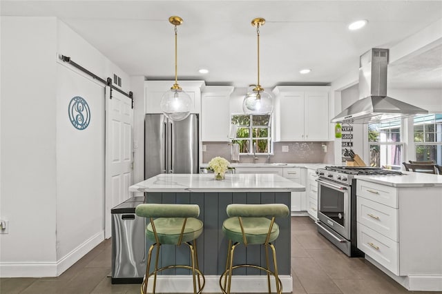 kitchen featuring a barn door, premium appliances, white cabinetry, backsplash, and exhaust hood