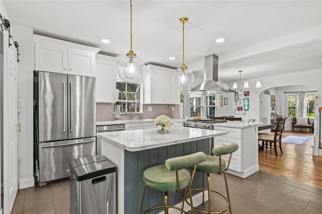 kitchen featuring arched walkways, island range hood, a peninsula, appliances with stainless steel finishes, and a center island