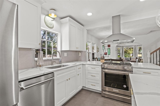 kitchen with tasteful backsplash, appliances with stainless steel finishes, white cabinetry, a sink, and island range hood