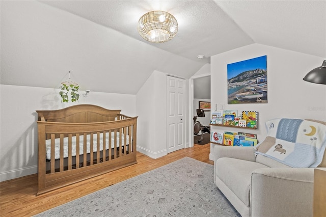 bedroom featuring a crib, baseboards, lofted ceiling, wood finished floors, and a textured ceiling