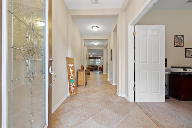 hallway featuring visible vents, light carpet, baseboards, and light tile patterned floors