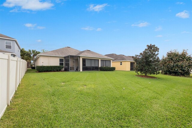 rear view of property featuring a lawn, fence, and a sunroom
