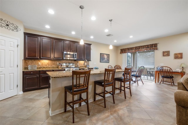 kitchen featuring light stone countertops, a breakfast bar area, stove, stainless steel microwave, and tasteful backsplash