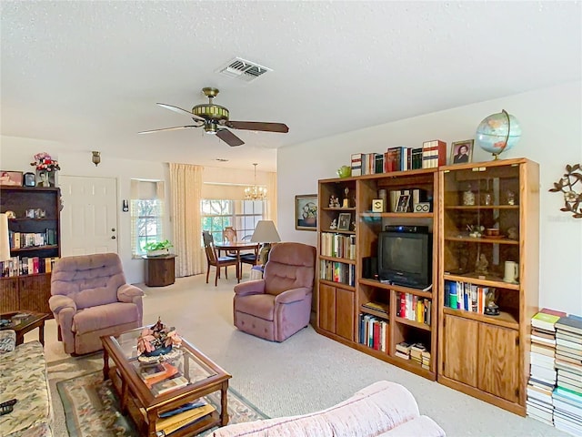 carpeted living area with visible vents, a textured ceiling, and ceiling fan with notable chandelier