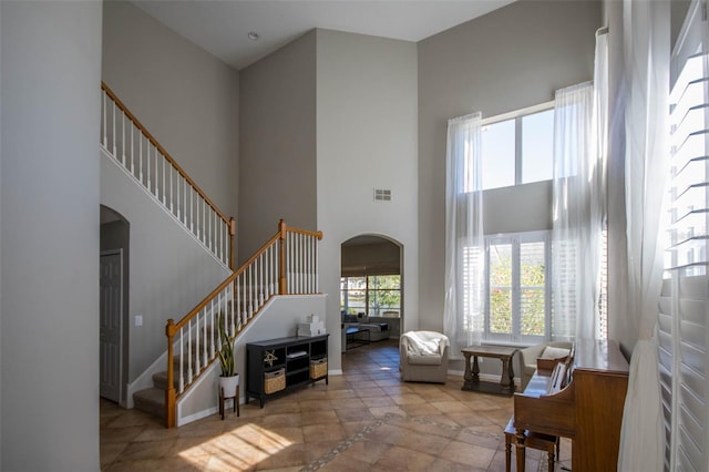 living room with arched walkways, a towering ceiling, visible vents, stairs, and baseboards