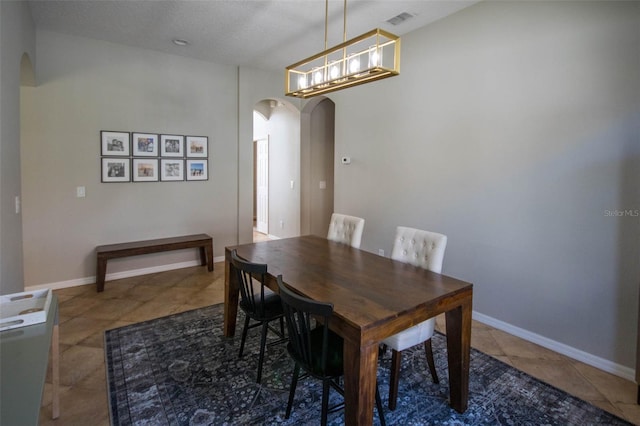 tiled dining area featuring arched walkways, a textured ceiling, visible vents, and baseboards