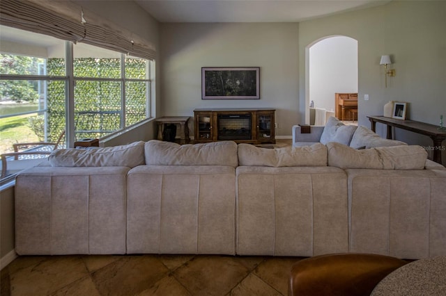 living room featuring arched walkways, a glass covered fireplace, and baseboards