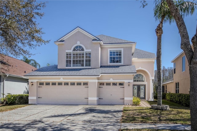 traditional home with a garage, driveway, a shingled roof, and stucco siding