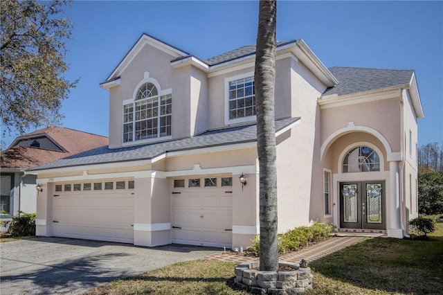 traditional home featuring french doors, roof with shingles, an attached garage, and stucco siding