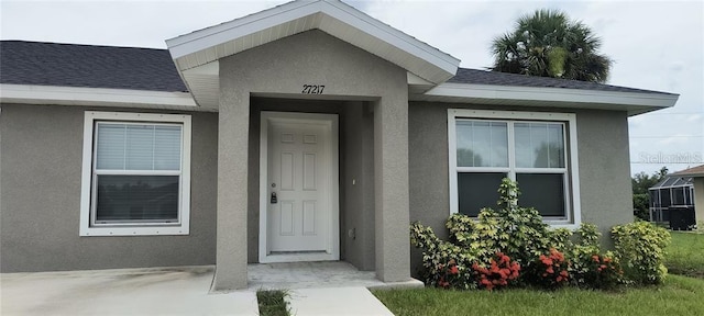 property entrance featuring stucco siding and roof with shingles