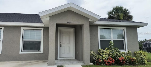 view of exterior entry with stucco siding and a shingled roof