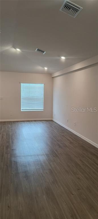 empty room with dark wood finished floors, baseboards, and visible vents