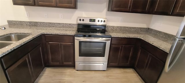 kitchen featuring light stone counters, light wood-style flooring, a sink, stainless steel appliances, and dark brown cabinets