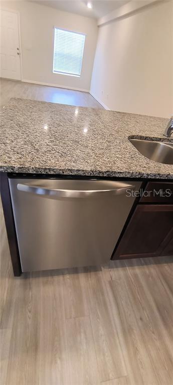 kitchen featuring stainless steel dishwasher, dark stone countertops, light wood-style flooring, and a sink