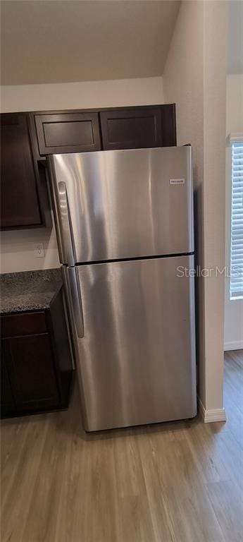 kitchen with dark brown cabinetry, light wood-type flooring, freestanding refrigerator, and baseboards