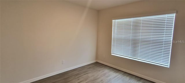 empty room featuring wood finished floors, a healthy amount of sunlight, and baseboards