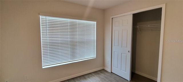 unfurnished bedroom featuring wood finished floors, baseboards, and a closet