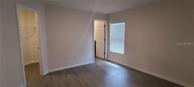 unfurnished bedroom with a spacious closet, wood finished floors, baseboards, and a closet