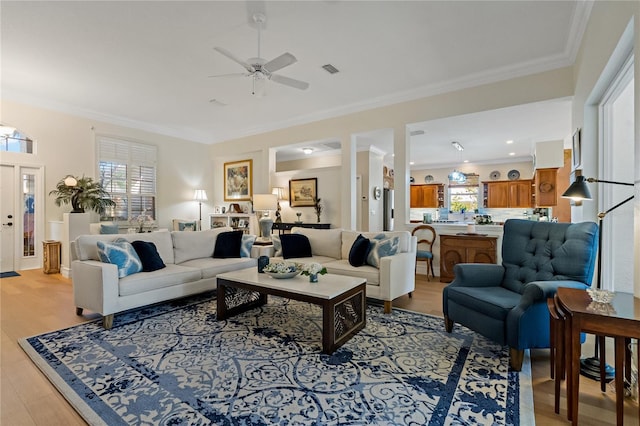 living room featuring ornamental molding, light wood-type flooring, visible vents, and ceiling fan