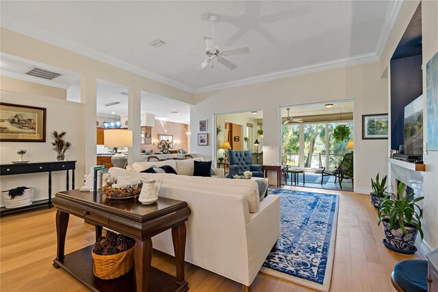 living room with light wood finished floors, visible vents, baseboards, ceiling fan, and ornamental molding