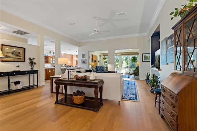 living room with light wood-type flooring, ceiling fan, visible vents, and crown molding