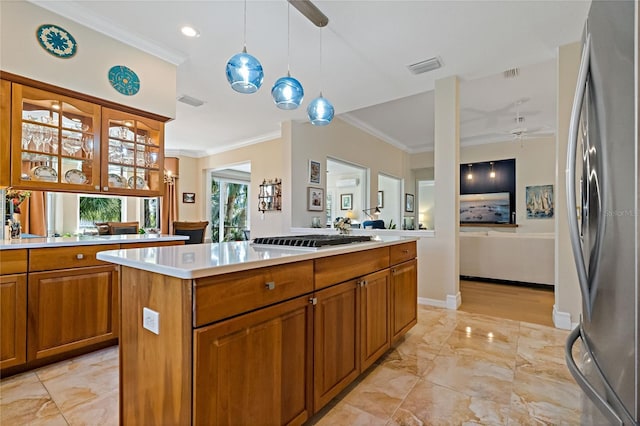 kitchen with brown cabinetry, freestanding refrigerator, ornamental molding, ceiling fan, and a kitchen island