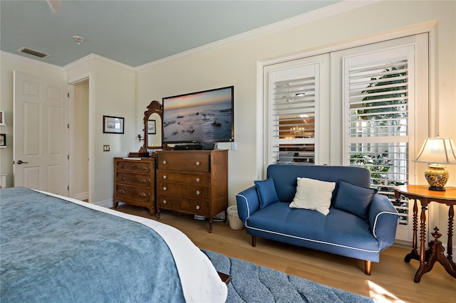 bedroom with baseboards, wood finished floors, visible vents, and crown molding