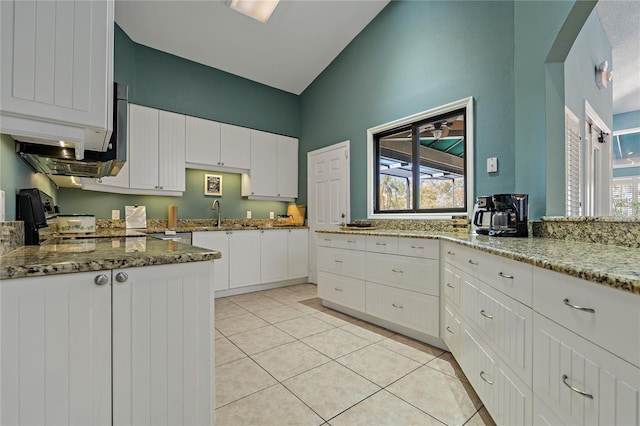 kitchen with light tile patterned flooring, stone countertops, stove, white cabinetry, and a wealth of natural light