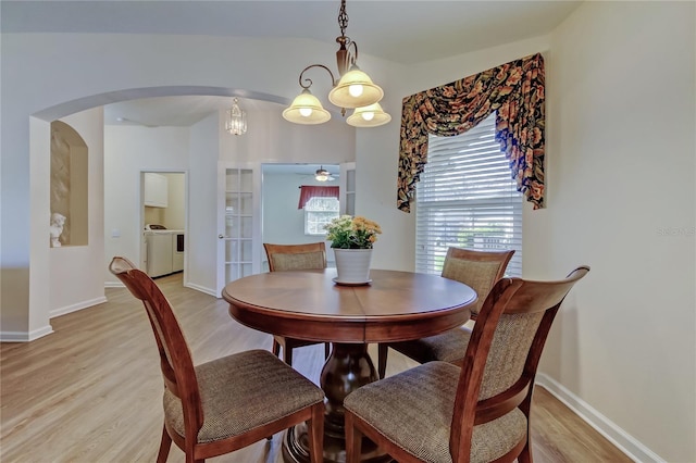 dining area with light wood-style floors, arched walkways, a healthy amount of sunlight, and washing machine and clothes dryer