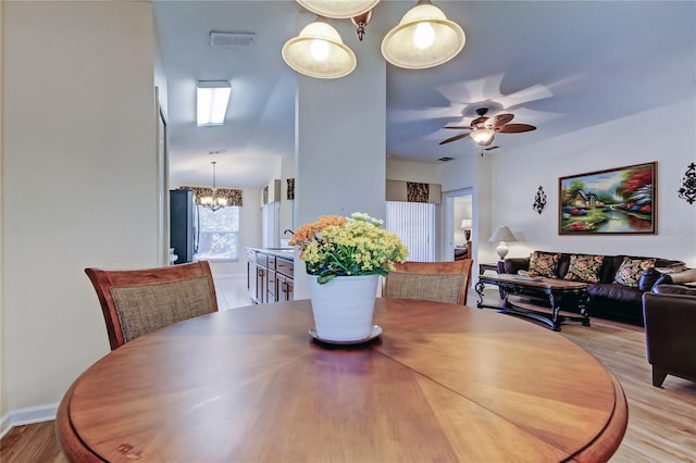 dining area with light wood-type flooring, visible vents, and ceiling fan with notable chandelier