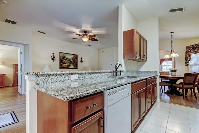 kitchen with light stone counters, visible vents, white dishwasher, a sink, and a peninsula