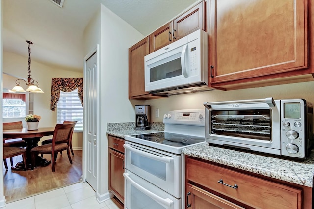 kitchen featuring light stone counters, a toaster, white appliances, brown cabinetry, and decorative light fixtures