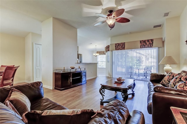 living area with ceiling fan with notable chandelier, visible vents, baseboards, and wood finished floors