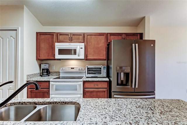 kitchen featuring light stone countertops, a toaster, white appliances, a sink, and brown cabinets