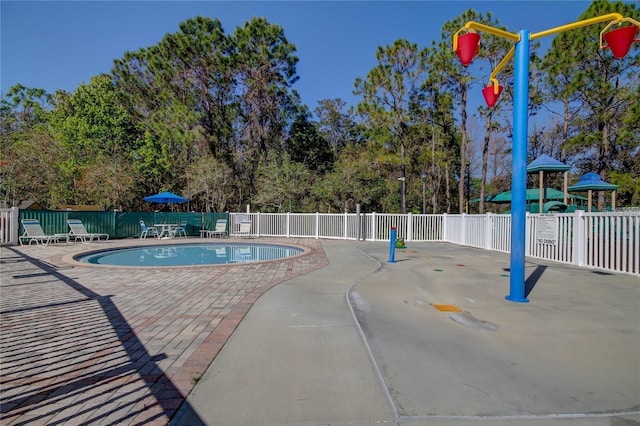 community pool with a patio area, fence, and playground community