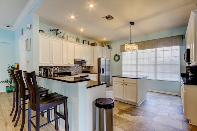 kitchen featuring visible vents, a kitchen island, a peninsula, under cabinet range hood, and stainless steel fridge with ice dispenser