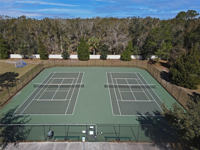 view of tennis court with a forest view and fence