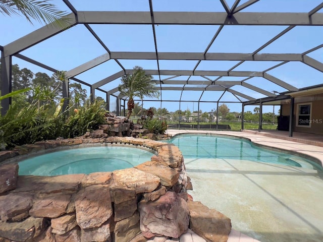 pool with glass enclosure, a patio area, and an in ground hot tub