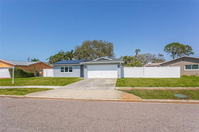 view of front of house featuring solar panels, concrete driveway, a front lawn, and fence