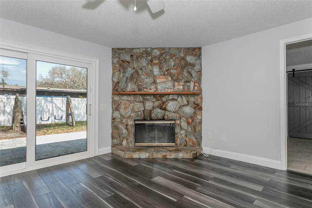 unfurnished living room with a textured ceiling, wood finished floors, a barn door, a fireplace, and baseboards