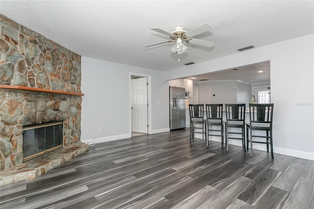 unfurnished living room with visible vents, dark wood-type flooring, a stone fireplace, and a textured ceiling