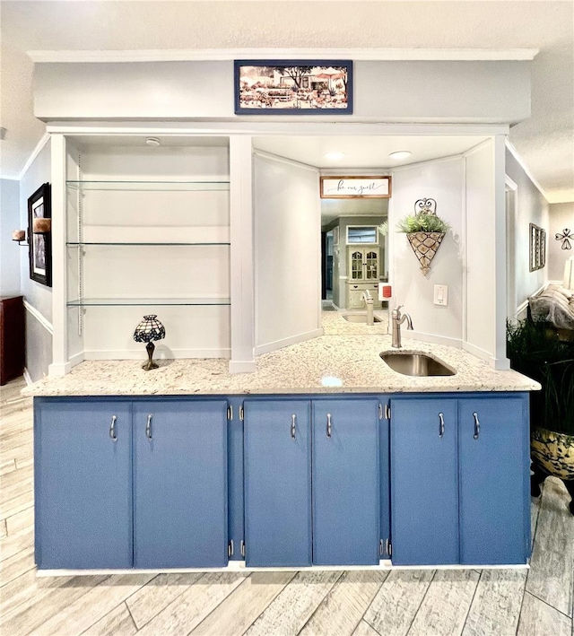 kitchen with blue cabinets, light stone counters, crown molding, and a sink