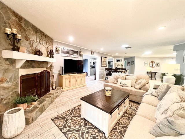 living room featuring a stone fireplace, ornamental molding, wood finished floors, and a textured ceiling