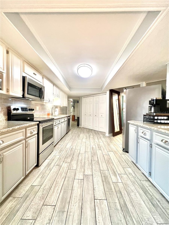 kitchen featuring wood finish floors, a sink, decorative backsplash, ornamental molding, and stainless steel appliances