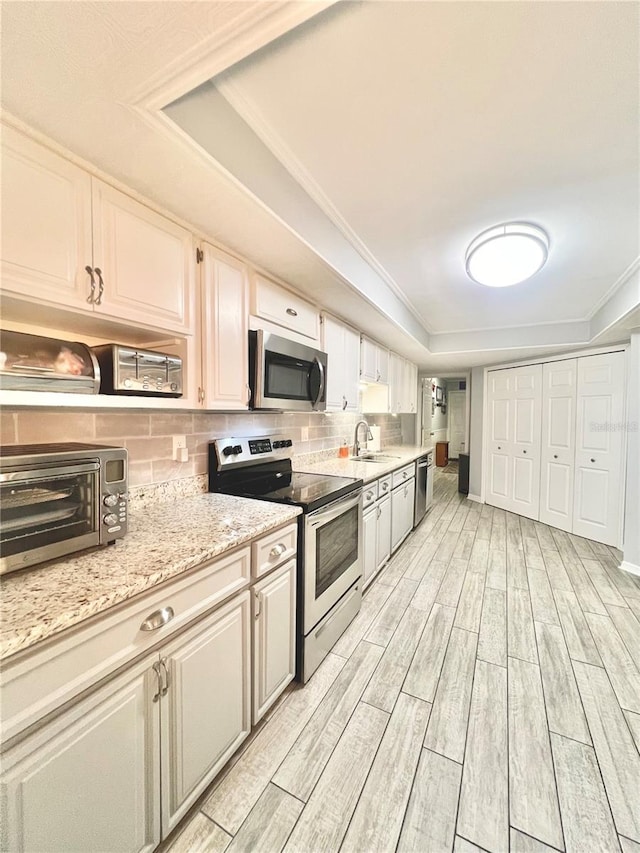 kitchen featuring wood finish floors, a sink, tasteful backsplash, stainless steel appliances, and a raised ceiling