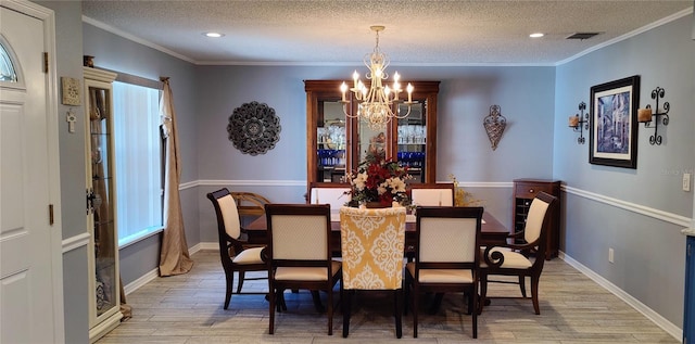 dining room featuring a textured ceiling, a notable chandelier, light wood-style floors, and ornamental molding