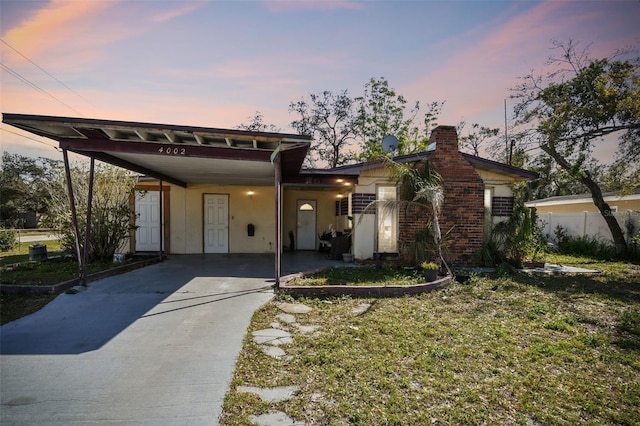 view of front of house with a carport, concrete driveway, fence, and a chimney