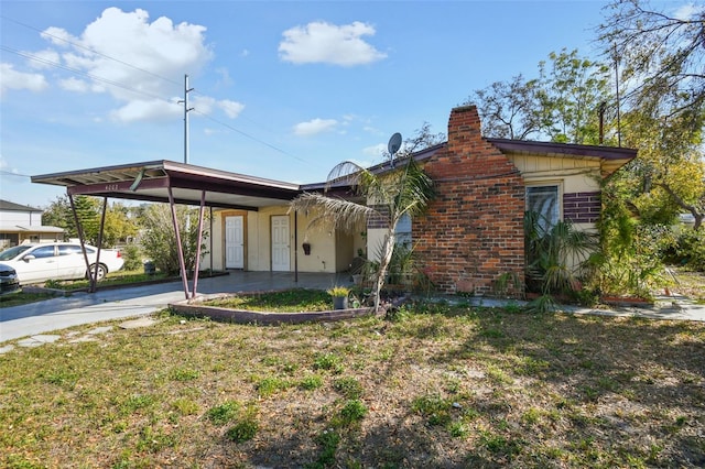 view of front facade featuring driveway, a chimney, a carport, and brick siding