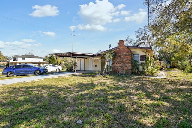 view of front of house featuring driveway, a chimney, a front yard, a carport, and brick siding